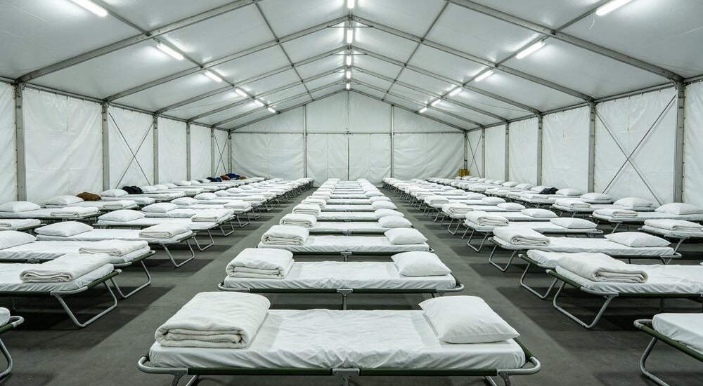 Large emergency shelter hall with rows of beds and institutional bedding