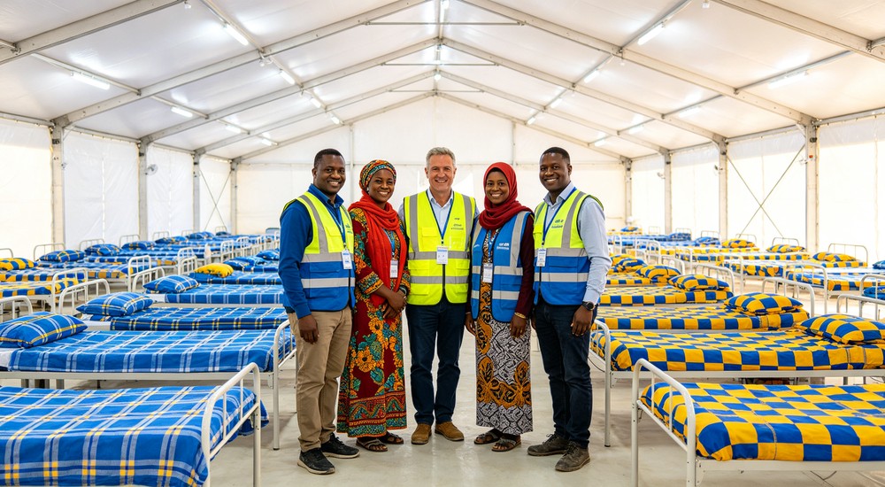 Side-by-side bright emergency relief tent interior with rows of metal beds featuring blue and yellow checkered bedding and aid workers