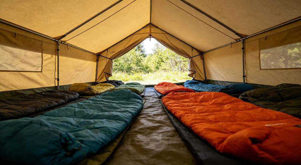 Wide angle view of tent interior with sleeping bags arranged, outdoor semi-exposed emergency shelter condition, natural daylight inside tent Wide angle view of tent interior with sleeping bags arranged, outdoor semi-exposed emergency shelter condition, natural daylight inside tent