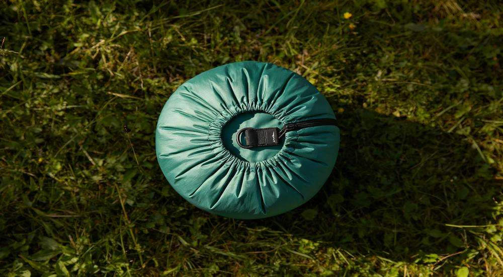 Top view of sleeping bag compression sack accessory, compact storage solution, outdoor gear display on grass Top view of sleeping bag compression sack accessory, compact storage solution, outdoor gear display on grass