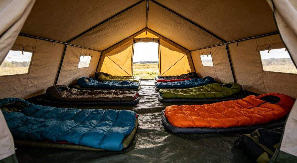 Wide angle view of tent interior with multiple sleeping bags arranged outdoor semi-exposed emergency shelter