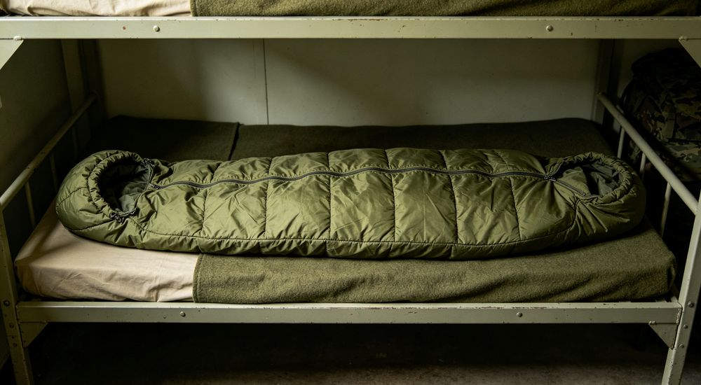 Medium shot inside bright tent with warm sunlight - person sleeping comfortably inside emergency sleeping bag, disaster relief shelter scene, cozy realistic photography