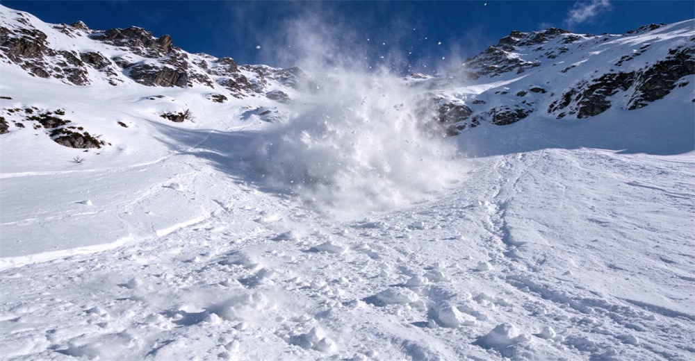 Wide dramatic view of snowy mountain avalanche path with broken snow debris showing backcountry avalanche risk and rescue terrain