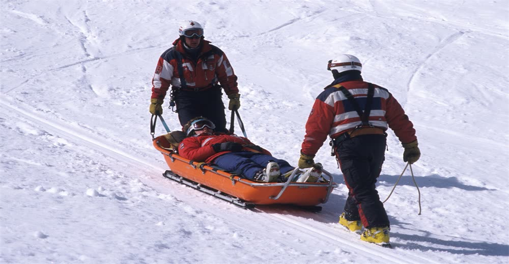 Wide view of rescuers pulling injured skier on rescue sled across snowy slope showing patient evacuation